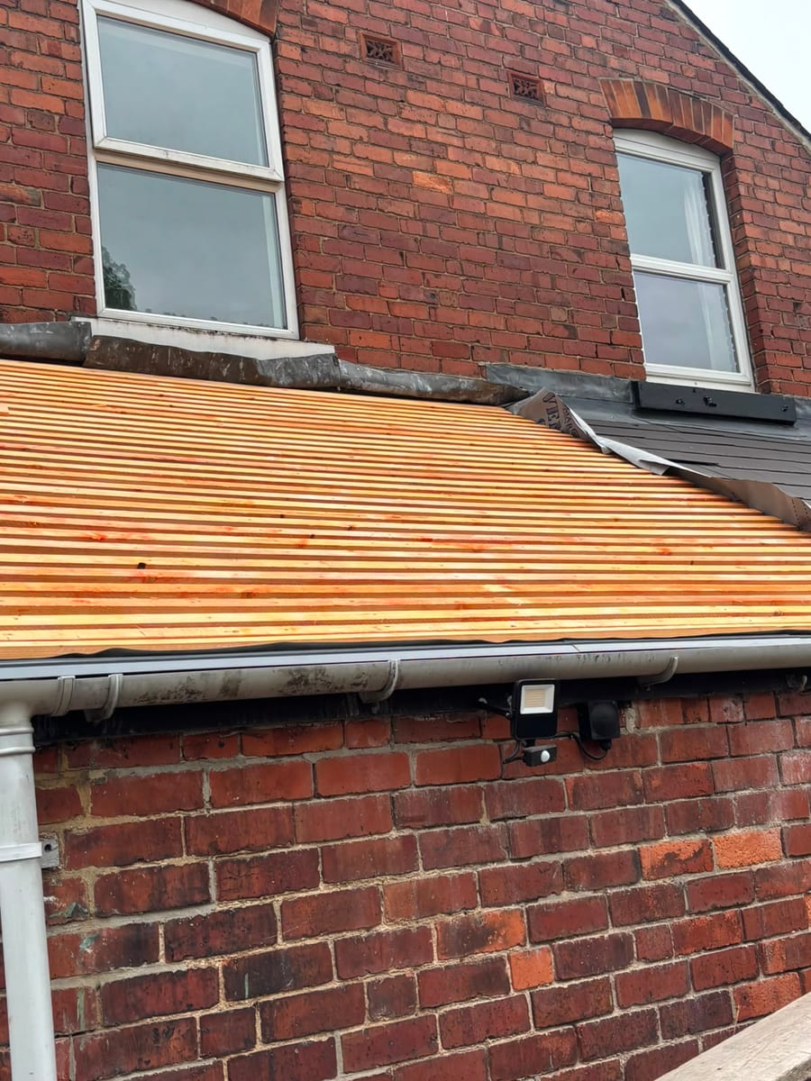New timber roof battens on a lower pitched roof, with roof covering being fitted beside the brick house