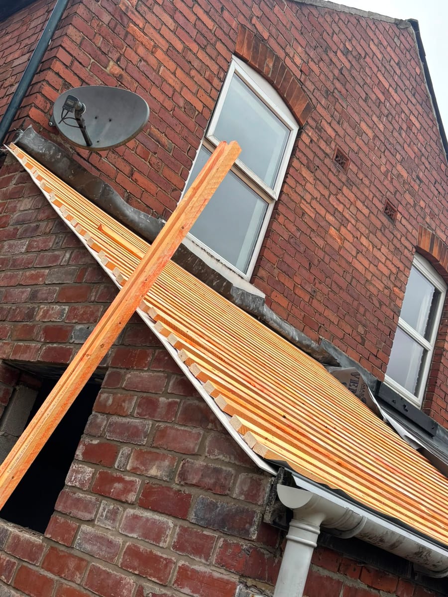 Side view of the lower pitched roof showing new timber battens and existing lead flashing against the brick wall